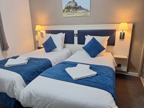 Twin bedroom at Hôtel les Alizés with blue and white bedding, wall lamps, and Mont Saint-Michel artwork above headboard