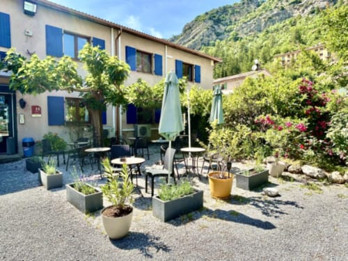 Hôtel les Alizés courtyard in Puget-Théniers with outdoor seating, potted plants, umbrellas, and mountain views