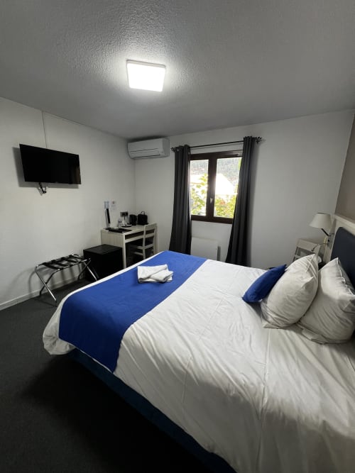 Camera moderna dell'Hôtel les Alizés a Puget-Théniers con letto queen-size, scappalaie blu, TV a parete e scrivania di lavoro