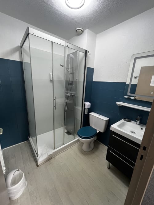 Bagno moderno all'Hôtel les Alizés con doccia in vetro, piastrelle blu, lavandino bianco e sedile del wc blu