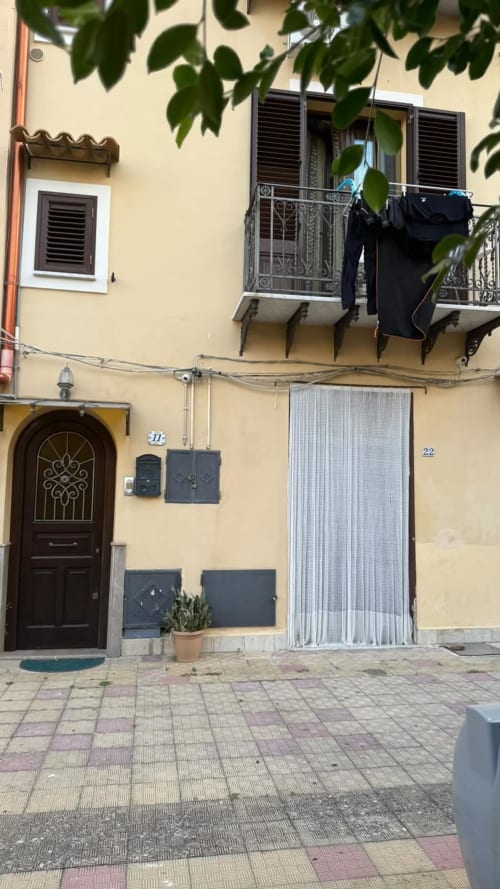Facciata gialla della Solunto Home Holiday a Santa Flavia con porta in legno ornato, balconate e muri ricoperti di edera