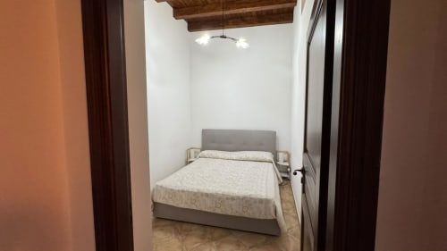 Camera moderna a Solunto Home Holiday a Santa Flavia con letto grigio, pareti bianche, travi in legno e TV a schermo piatto
