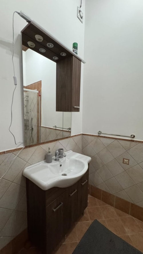 Bagno moderno della Solunto Home Holiday a Santa Flavia con lavabo bianco, mobile in legno scuro, ampio specchio illuminato e