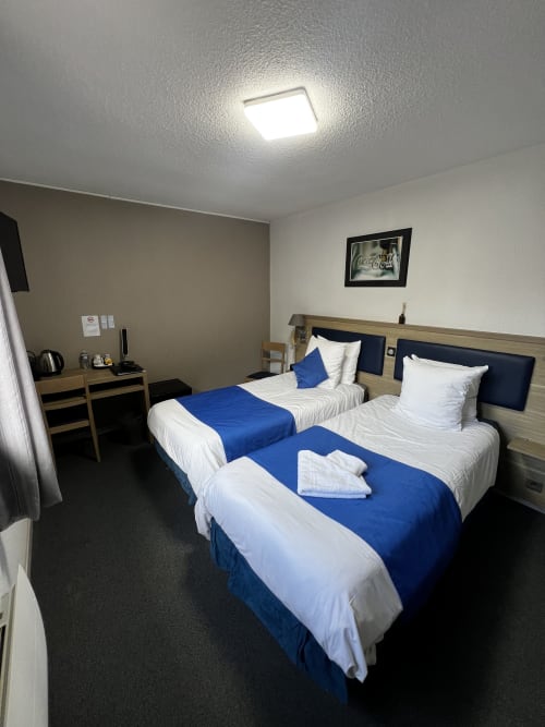 Twin bedroom at Hôtel les Alizés, Puget-Théniers with two beds, blue linens, work desk, and ceiling light