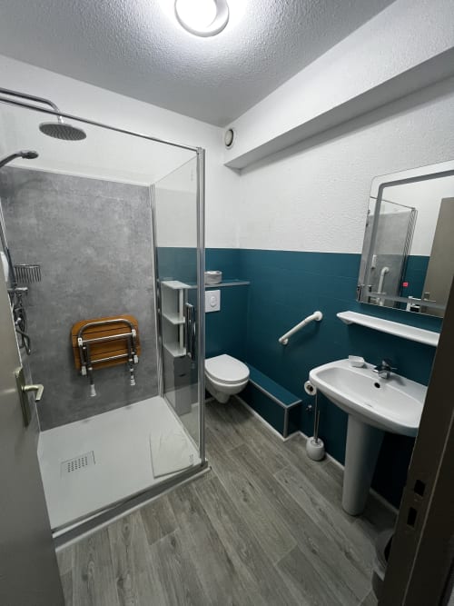 Bagno moderno dell'Hôtel les Alizés con doccia walk-in, WC, lavabo su colonna e caratteristiche di accessibilità incluse maniglie di sicurezza