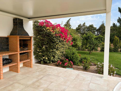 Pátio coberto com lareira de tijolos, flores de buganvília rosa e vista para o jardim na Quinta Vale da Paz, Azambuja