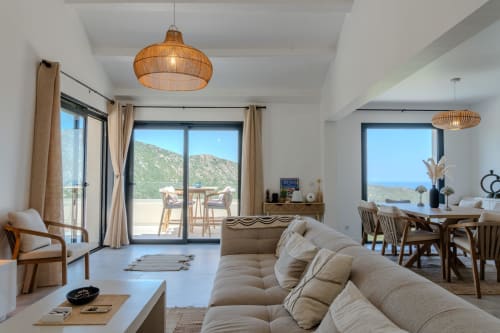 Villa Roya Saint-Florent: Modern living room with beige sofa, sea views, wooden furnishings, and woven pendant lights