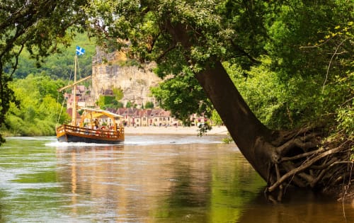 Bateau en bois sur la rivière avec bâtiments historiques et falaise au Clos Gaillardou, Dordogne France