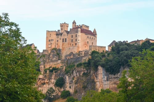 Château de style Neuschwanstein perché sur une falaise rocheuse entourée de forêt verdoyante en Dordogne, France