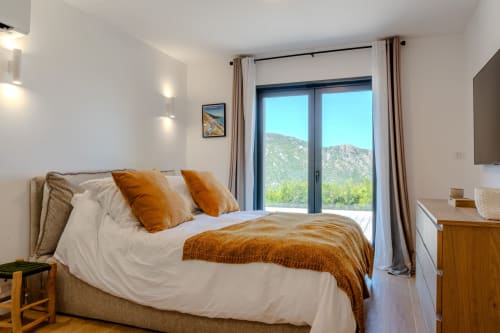 Chambre moderne à la Villa Roya à Saint-Florent avec vue montagne, accents orangés et mobilier contemporain
