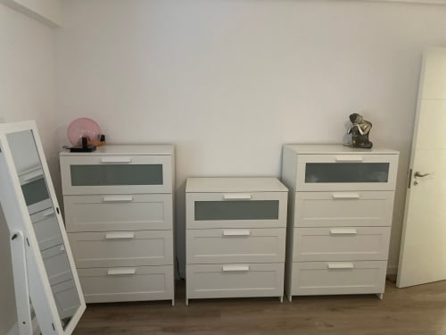 Tres cómodas blancas con frentes de cajones oscuros en el apartamento Algemesi Home, decoradas con objetos decorativos
