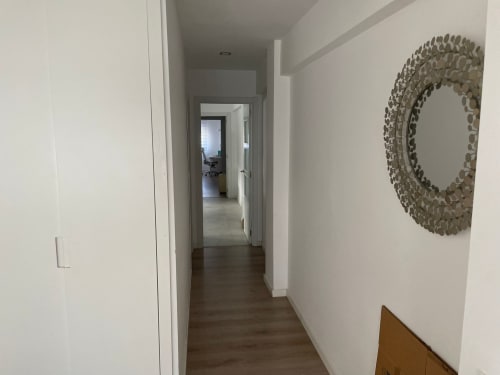Pasillo moderno con suelos de madera y espejo circular decorativo en apartamento de Algemesi con vistas a la ciudad