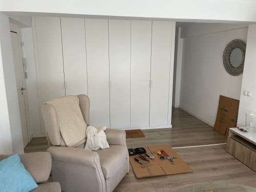 Dormitorio moderno con sillón beige, armarios empotrados blancos, suelo de madera y vistas a la ciudad en el apartamento Algemesi Home Valencia