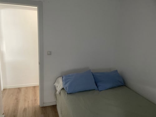 Dormitorio minimalista con almohadas azules en la cama, puerta abierta, suelo de madera y paredes grises en Algemesi Home Valencia