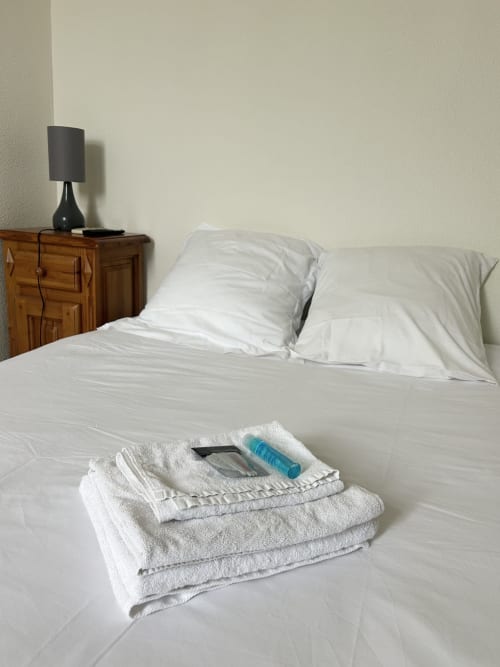 Chambre de l'hôtel BDM avec literie blanche, oreillers, serviettes sur le lit et table de nuit en bois avec lampe noire
