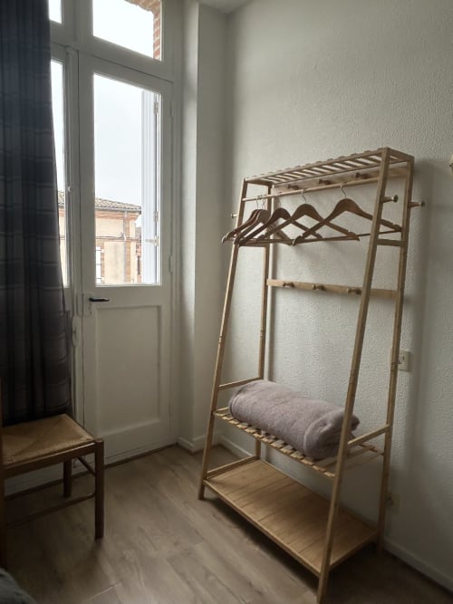 Portant à vêtements en bois avec cintres dans la chambre lumineuse de l'Hôtel BDM, Montastruc-la-Conseillère, avec vue sur la ville