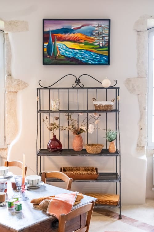 Salle à manger du Jardin Secret à Grignan avec étagères en fer forgé, œuvres d'art colorées et table de petit-déjeuner