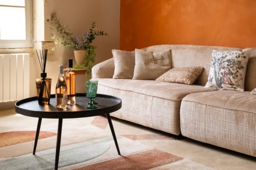 Salon cosy du Jardin Secret à Grignan avec canapé beige, table basse noire et mur d'accent orange chaleureux