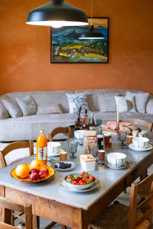 Table du petit-déjeuner au Jardin Secret à Grignan, avec fruits, salade fraîche et jus d'orange sous des lampes suspendues noires