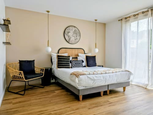 Chambre moderne à La Clairière aux Chênes avec tête de lit en rotin, luminaires suspendus et fauteuil lounge