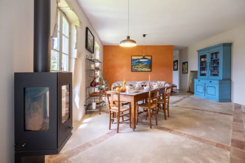 Spacieuse salle à manger du Jardin Secret à Grignan avec mur d'accent orange, table en bois, cheminée et buffet bleu