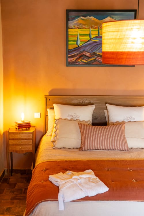 Chambre chaleureuse au Le Jardin Secret B&B à Grignan avec lit en bois, oreillers blancs et tableau paysage toscan