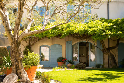 Cour charmante du Jardin Secret à Grignan avec arbre ombragé, portes bleues et pelouse verdoyante