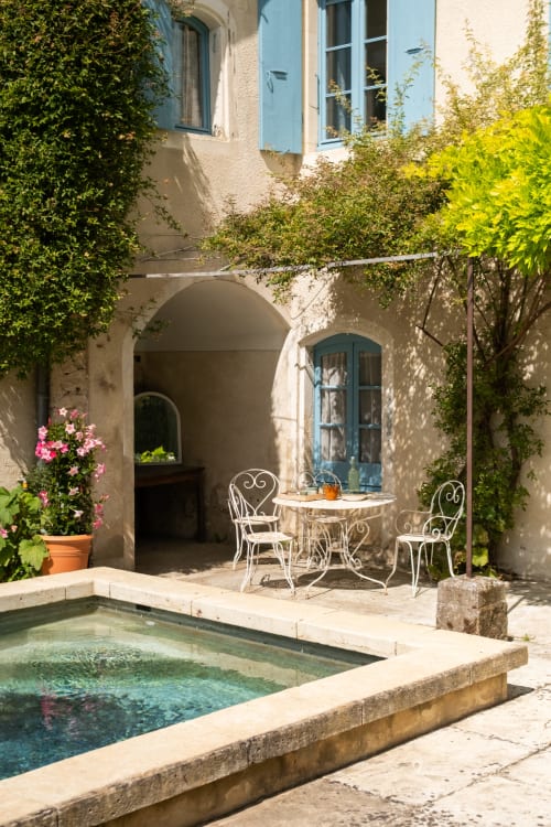 Charmante cour du Jardin Secret avec piscine, sièges en fer forgé et arches couvertes de lierre à Grignan