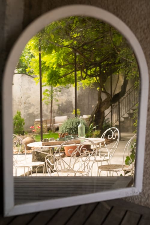 Porche voûté encadrant une élégante cour avec mobilier en fer forgé et verdure luxuriante au Jardin Secret de Grignan