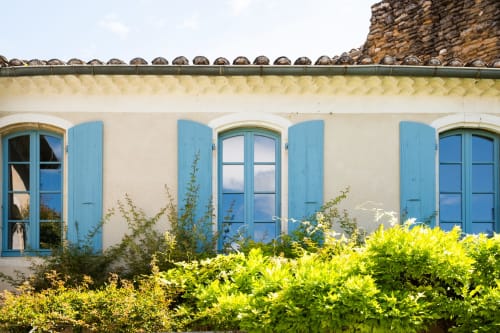 Façade aux volets bleus de Le Jardin Secret B&B à Grignan, avec haies verdoyantes et fenêtres en arc