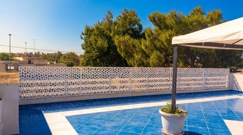 Terrazza esterna della Aura Luxury Villa con patio in piastrelle blu, eleganti schermi bianchi per la privacy e alberi lussureggianti a My Home Apulia