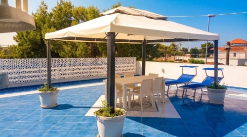 Terrazza soleggiata a bordo piscina di My Home Apulia con pergolato, tavolo da pranzo, lettini e viste sul giardino