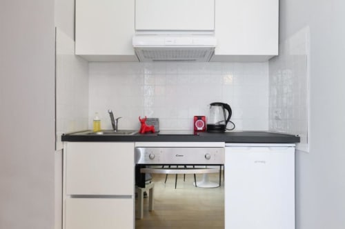Cucina bianca moderna con piano in nero, forno in acciaio inox e bollitore rosso nell'appartamento milanese ACasaDiImma
