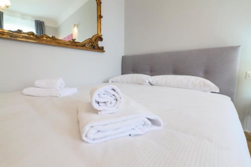Camera da letto moderna dell'appartamento ACasaDiImma a Milano con testata grigia, lenzuola bianche e asciugamani arrotolati sul letto