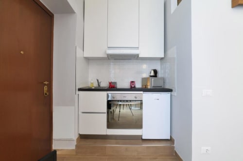 Kitchenette moderna con mobili bianchi, piano cottura nero e elettrodomestici in acciaio inox nell'appartamento ACasaDiImma a Milano