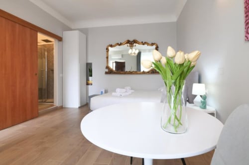 Elegante camera da letto milanese con tulipani bianchi su tavolo rotondo, specchio ornamentale e pavimento in legno presso ACasaDiImma