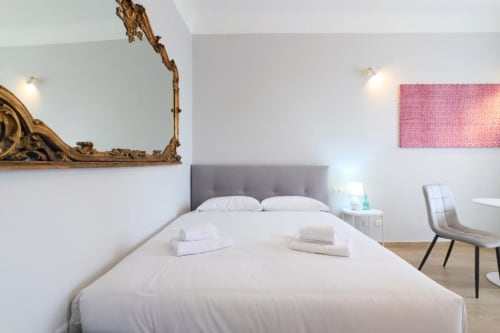 Camera da letto moderna a Milano con biancheria bianca, testata grigia, specchio dorato ornamentale e opera d'arte rosa presso ACasaDiImma