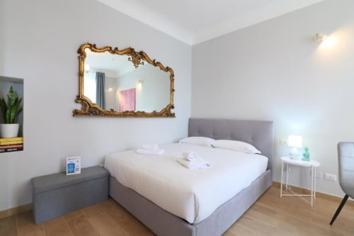 Camera moderna di ACasaDiImma Milano con letto grigio, specchio dorato ornamentale e pavimenti in legno