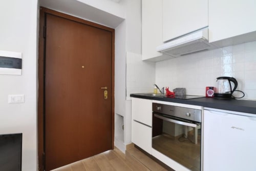 Cucina moderna nell'appartamento di Milano con porta d'ingresso marrone, mobili bianchi, piano cottura nero e elettrodomestici in acciaio inossidabile