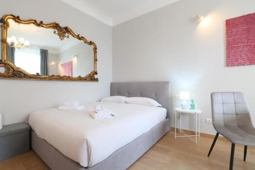 Camera da letto di appartamento moderno a Milano con letto imbottito grigio, specchio dorato ornamentale e arte decorativa rosa