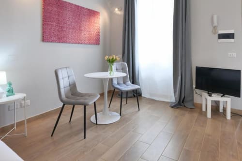 Soggiorno moderno in appartamento ad ACasaDiImma Milano con tavolo rotondo bianco, sedie grigie, opera d'arte rosa e pavimentazione in legno