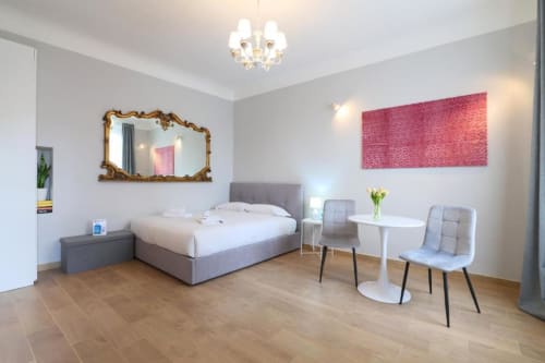 Camera moderna di ACasaDiImma Milano con letto grigio, specchio dorato, opera d'arte rosa e pavimenti in legno