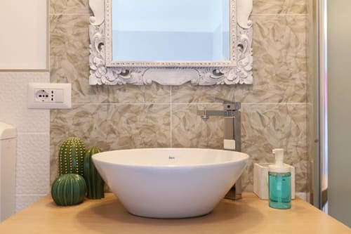 Bagno moderno presso ACasaDiImma Milano con lavabo bianco, specchio decorativo e piastrelle rivestite in marmo