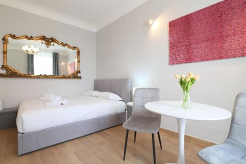 Camera da letto moderna a Milano con letto grigio, specchio oro ornamentale, parete rosa con arte texture e tavolino rotondo bianco con fiori