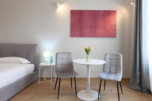 Camera da letto moderna a Milano con tavolo rotondo bianco, sedie grigie e opera d'arte astratta rossa sopra il letto