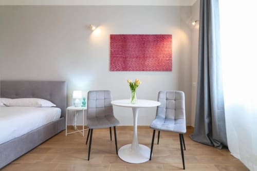 Camera da letto moderna in appartamento milanese con letto, tavolo rotondo bianco, sedie grigie, opera astratta rosa e pavimento in legno.