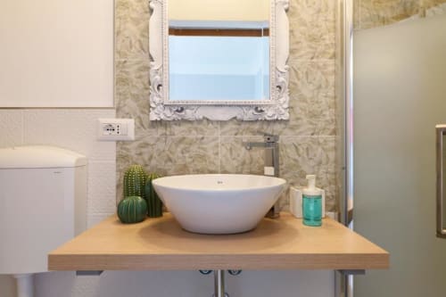 Vanità bagno moderno con lavabo bianco a bacinella, piano in legno, specchio decorativo e piante di cactus da ACasaDiImma Milano