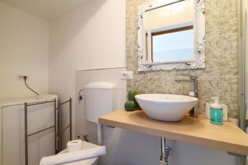 Bagno moderno nell'appartamento milanese con lavabo bianco a ciotola, specchio decorato, mobile in legno e bidet presso ACasaDiImma Navigli