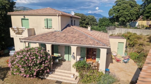 Gîte Mare e Monti à Vico avec toit en terre cuite, volets verts, fleurs roses et vue sur les montagnes