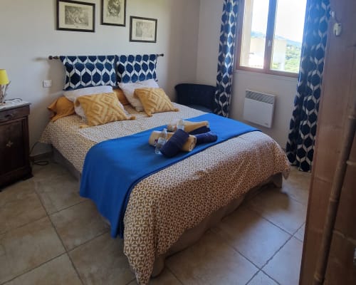 Chambre Ajaccio du B&B Mare e Monti à Vico, FR - lit queen-size avec chemin de lit bleu, coussins motifs et fenêtres avec vue mer